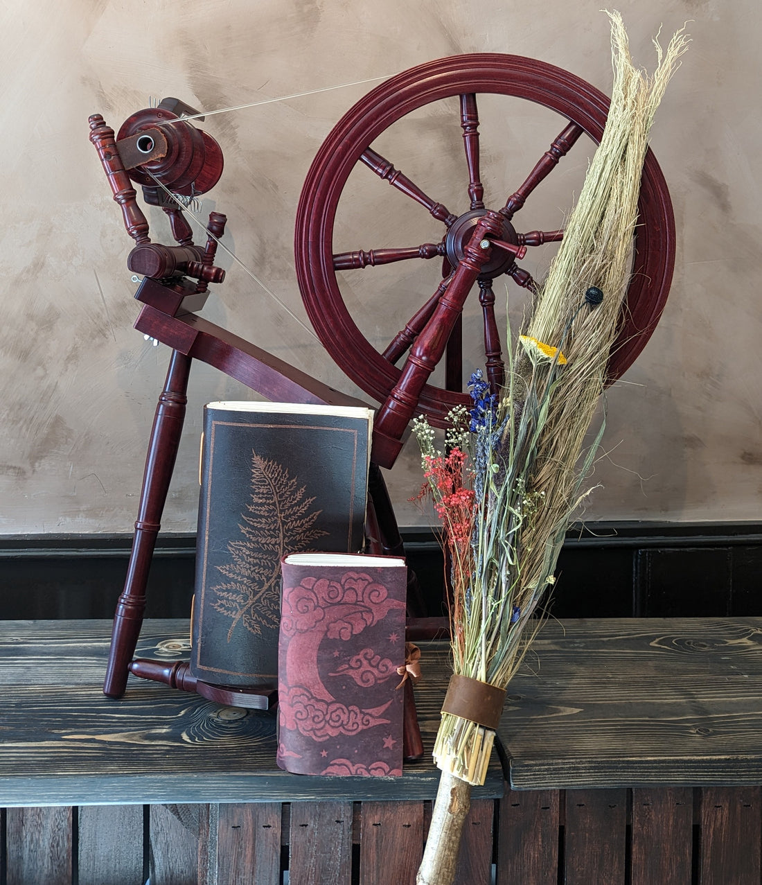 a spinning wheel, a broom, and two leatherbound journals