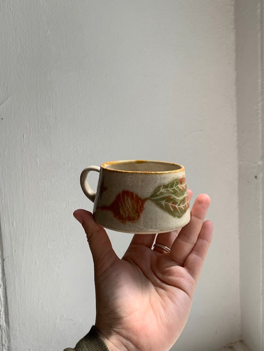 A mug in the sgraffito style held in a hand featuring a beetroot