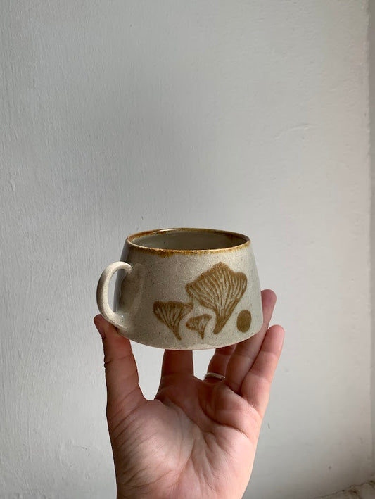 A mug in the sgraffito style held in a hand featuring a chantarelle mushroom